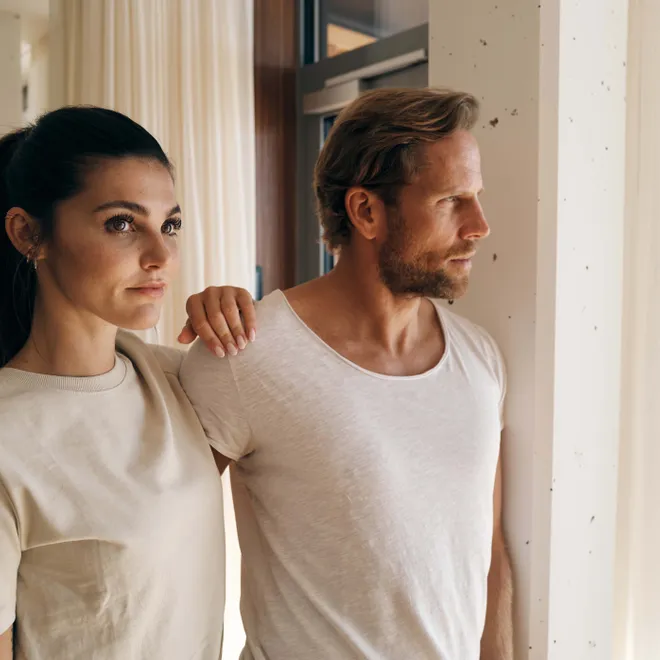 Couple in casual beige clothing gazing out a bright window in modern interior
