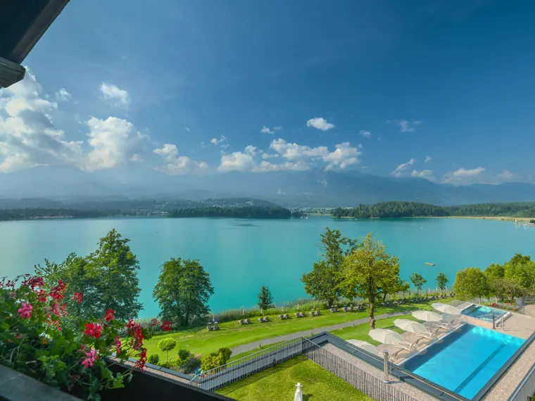 Panoramablick auf türkisfarbenen See, Berge, Pool und Garten vom Hotelbalkon