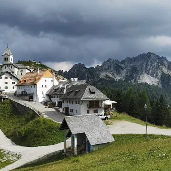 Bergdorf mit weißer Alpenkirche und Häusern unter dramatischem Wolkenhimmel