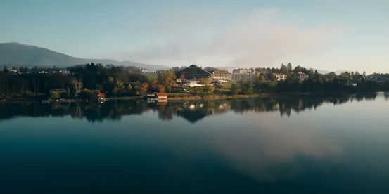 Hotels am See mit Spiegelung im Wasser und Bergen im Hintergrund