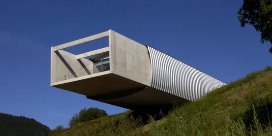 Modernes auskragendes Gebäude mit Beton- und Riffelmetallfassade an grasbewachsenem Hang