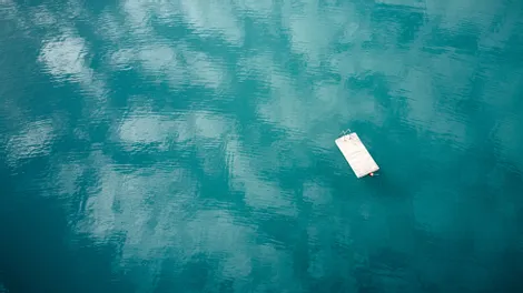 Schwimmender Holzsteg auf ruhigem türkisfarbenem See mit Himmelsreflexionen