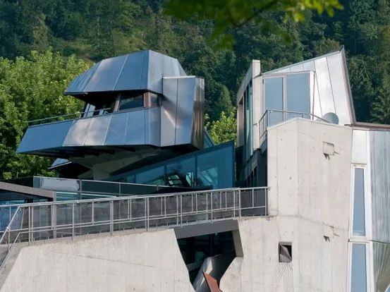 Moderne Architektur mit kantigen Metall- und Betonstrukturen vor bewaldetem Hügel