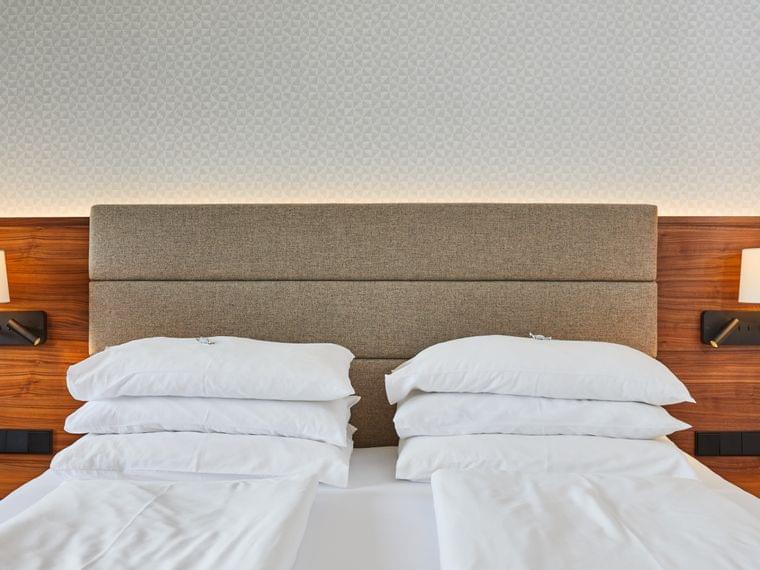 Modernes Hotelbett mit weißen Laken, Holzkopfteil und Wandlampen