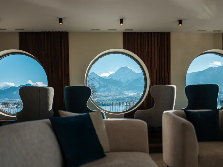 Lounge moderna con finestre circolari e vista panoramica sulle montagne alpine innevate