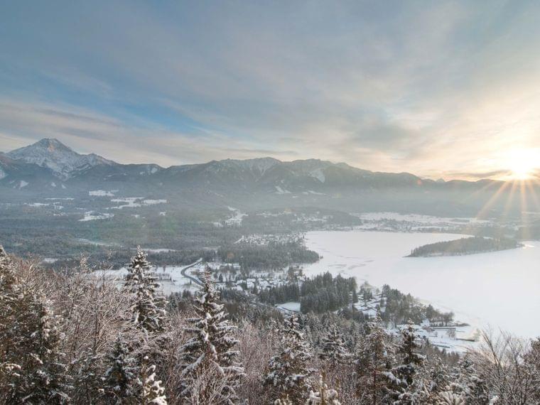 Paesaggio invernale con foresta innevata, lago ghiacciato e alba dietro la catena montuosa