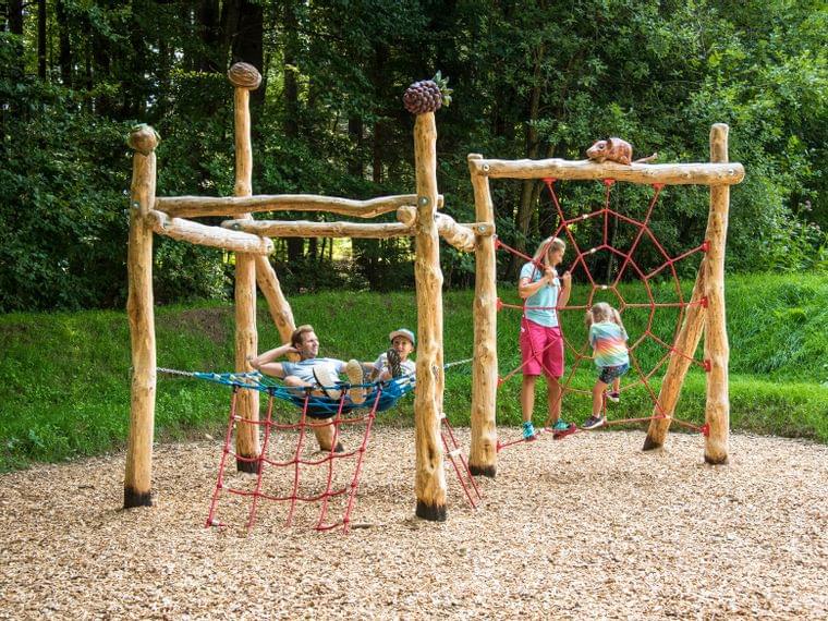 Familie spielt auf einem Spielplatz aus Holz mit Kletternetzen im Waldpark