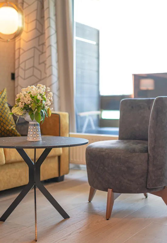 Modernes Wohnzimmer mit gelbem Sofa, grauem Stuhl und rundem Tisch mit Blumenvase