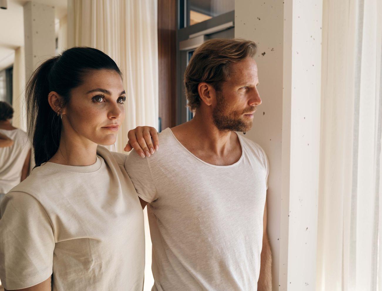 Couple in casual beige clothing gazing out a bright window in modern interior