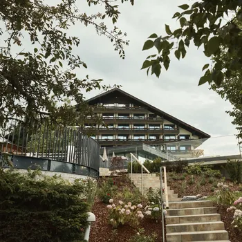 Alpenhotel mit Holzbalkonen in einem gepflegten Garten mit Steintreppe und blühenden Blumen