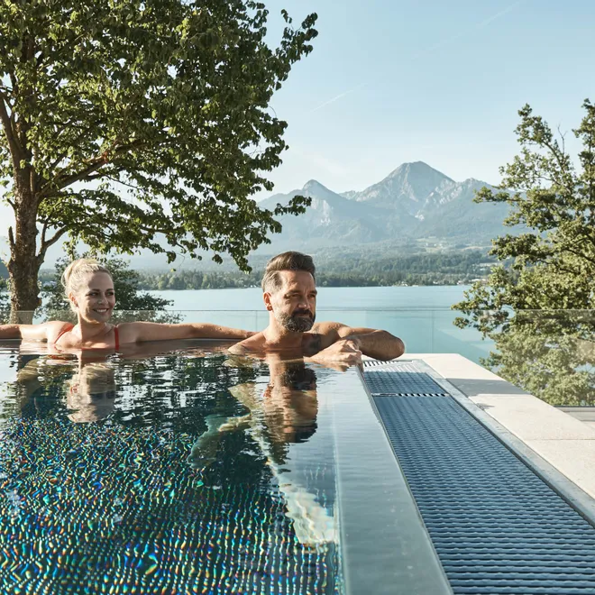 Paar entspannt im Infinity-Pool mit Blick auf See und Berge im Sommer