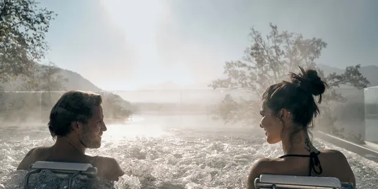 Couple relaxing in an outdoor hot tub with mountain view and morning sunlight
