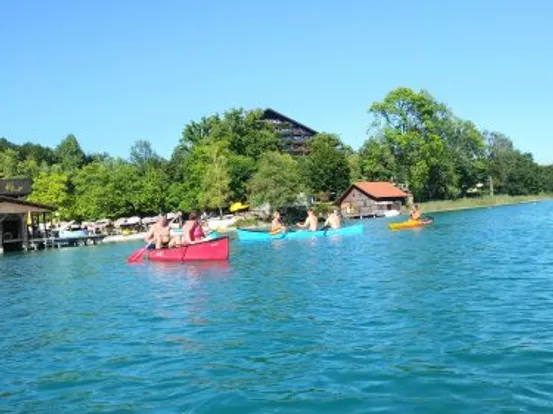 Menschen paddeln in bunten Booten auf einem klaren blauen See nahe Seehütten