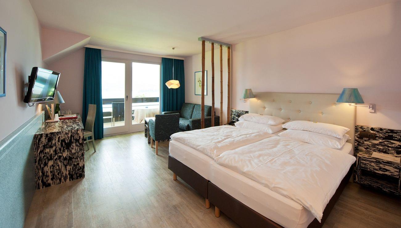 Modernes Hotelzimmer mit Doppelbett, Schreibtisch, Sitzecke und Zugang zum Balkon