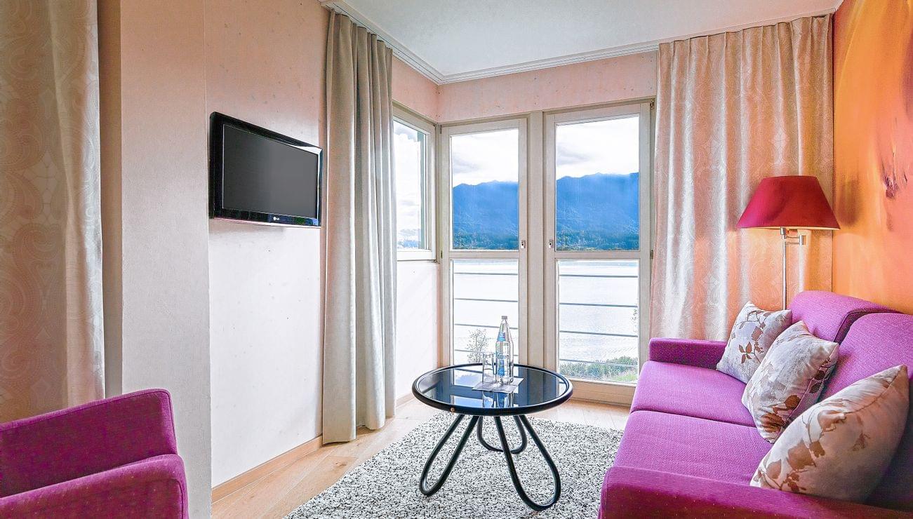 Moderna camera d'albergo con divani rosa, vista lago da grandi finestre e TV a parete