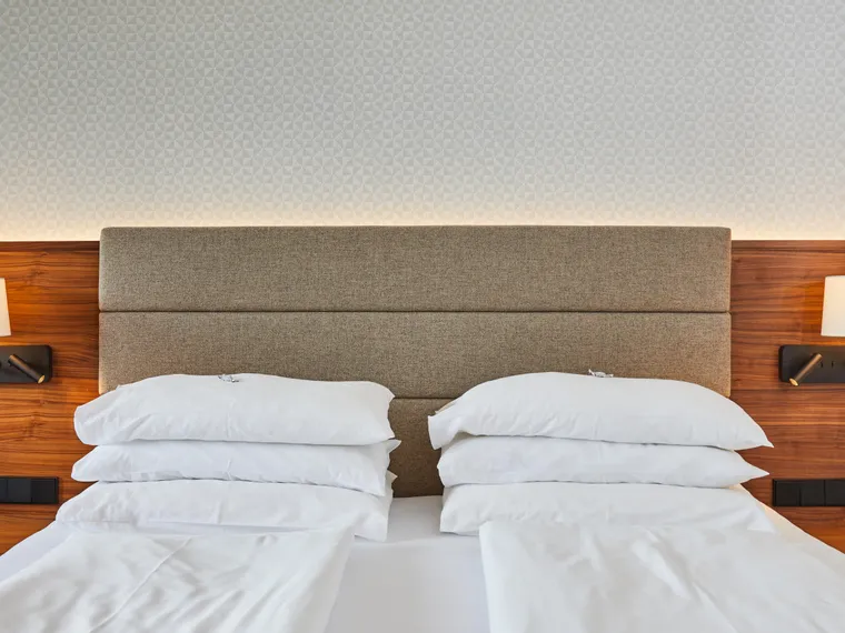 Modernes Hotelbett mit weißen Laken, Holzkopfteil und Wandlampen