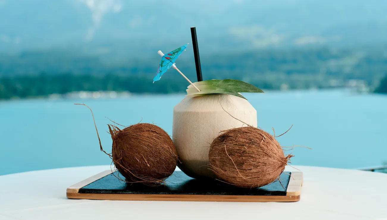 Bevanda di cocco con ombrellino e due noci di cocco su tavolo con vista lago e montagne