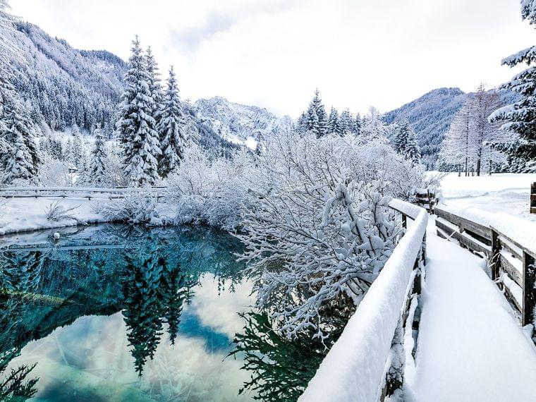 Sentiero di legno innevato accanto a un lago ghiacciato in una foresta alpina invernale