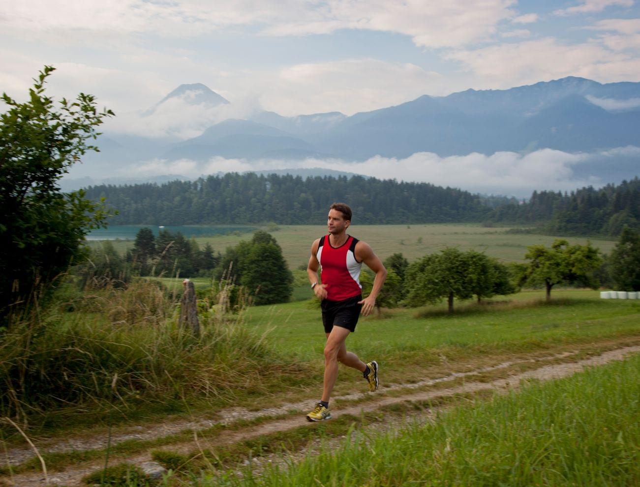 Mann joggt auf einem Landweg mit Bergen und Wald im Hintergrund