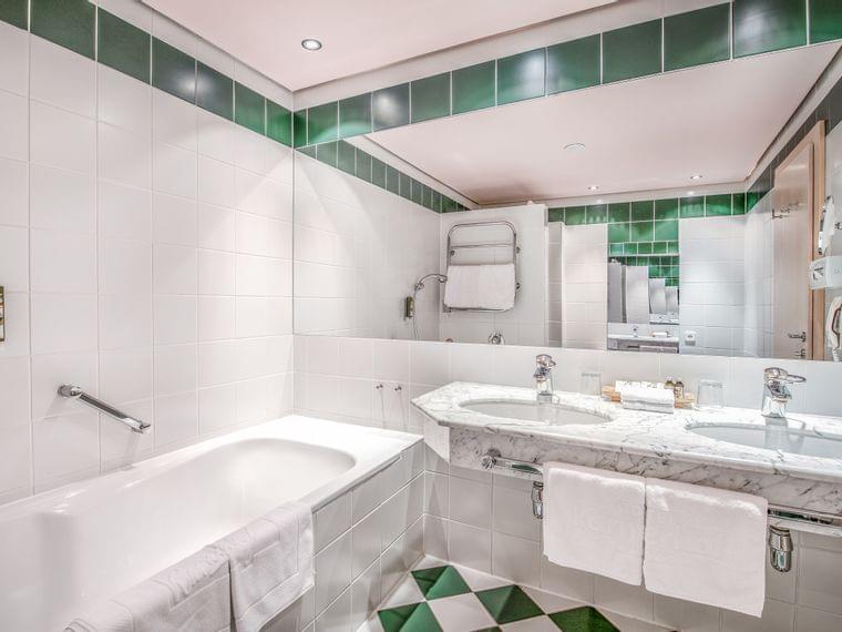 Modernes Hotelbad mit Doppelwaschbecken aus Marmor, Badewanne und grünen Fliesenakzenten