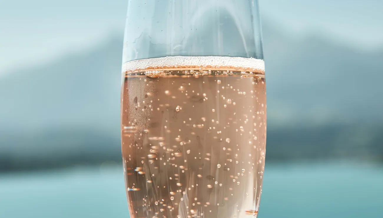 Glas mit Rosé-Sekt vor See und Bergen im Hintergrund