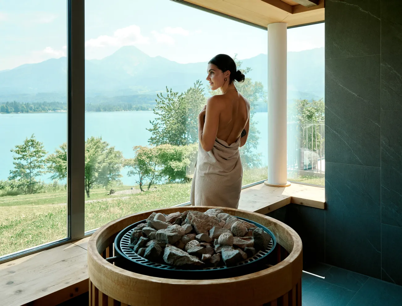 Frau im Handtuch genießt den Panoramablick auf den See aus der Sauna mit Steinofen