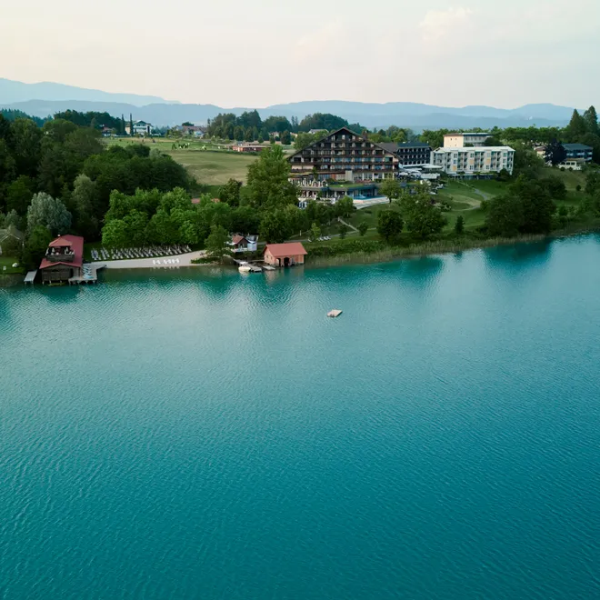 Resort sul lago con vegetazione rigogliosa e acqua blu limpida circondato da montagne