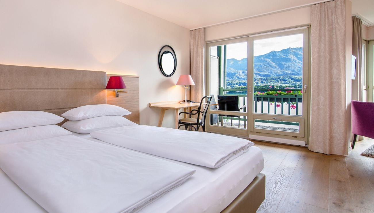 Camera d'albergo luminosa con letto matrimoniale, scrivania e vista montagna dal balcone