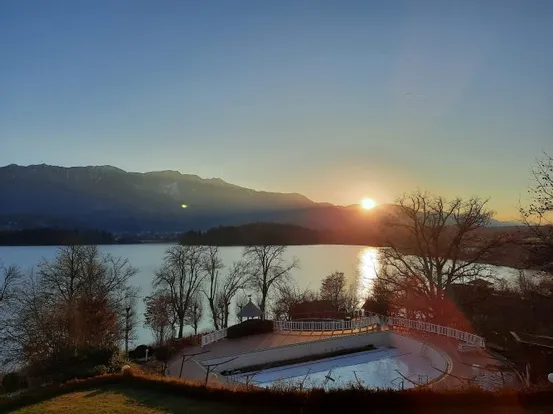 Sonnenuntergang über einem See mit Bergen im Hintergrund und Bäumen im Vordergrund