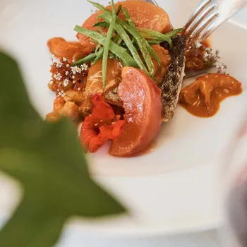 Gourmetgericht mit Fisch, Gemüse und essbaren Blüten in elegantem Restaurant