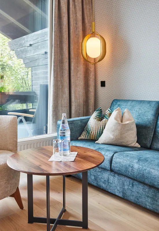 Gemütliche Hotellounge mit blauem Sofa, rundem Holztisch und Mineralwasser am Fenster