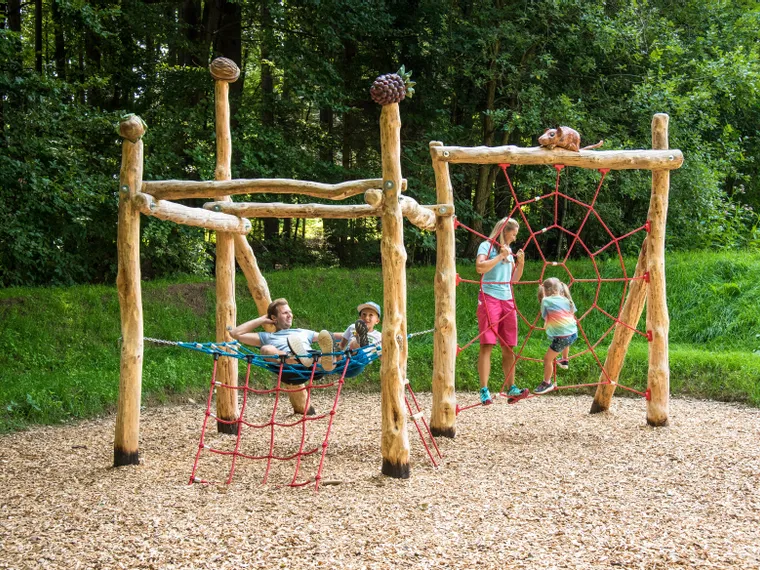 Family playing on a wooden playground with rope nets in a forest park