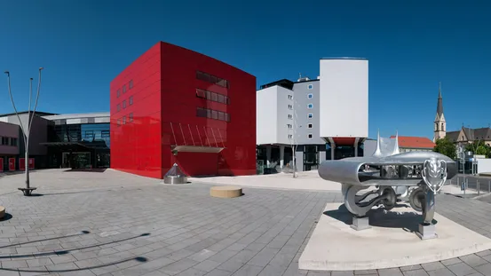 Moderne rote und weiße Gebäude mit Metallskulptur auf dem Platz unter klarem blauen Himmel