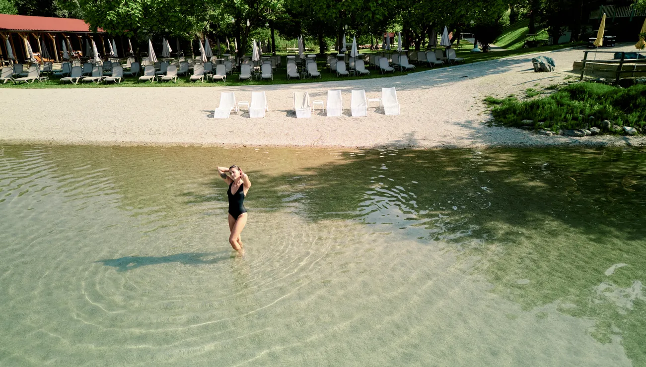 Frau im schwarzen Badeanzug steht im seichten Wasser eines Sees nahe Strandresort