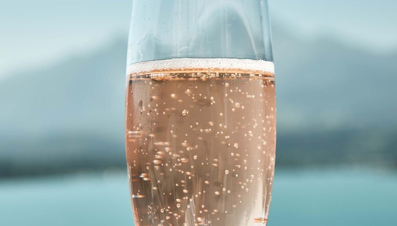 Bicchiere di vino rosé frizzante con lago e montagne sullo sfondo