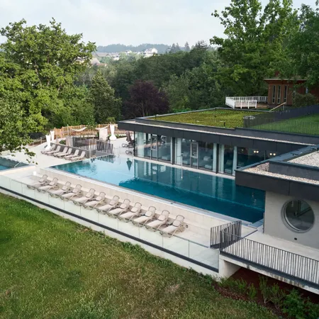 Modernes Wellnesshotel mit Infinity-Pool im Freien, Sonnenliegen und grüner Umgebung