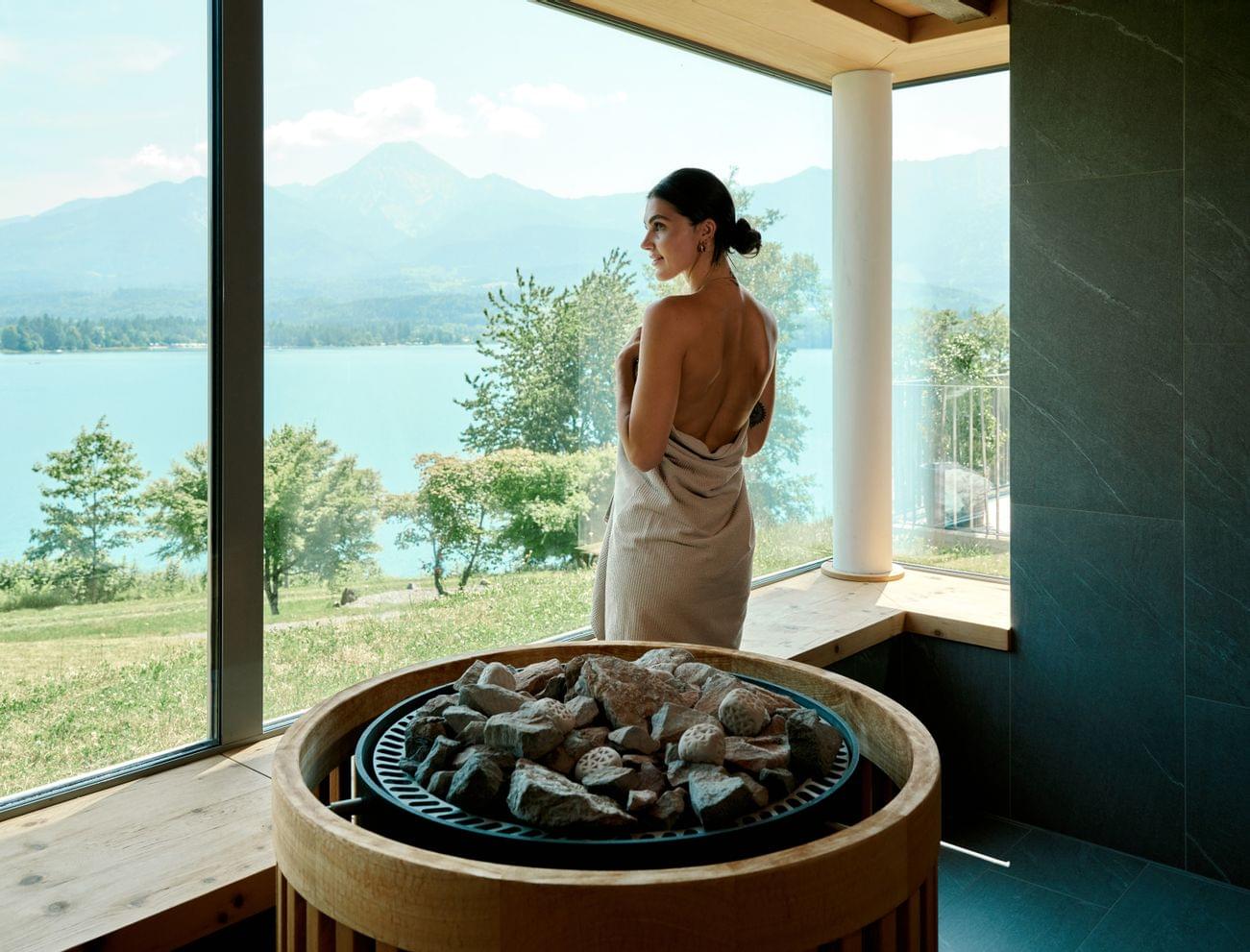 Frau im Handtuch genießt den Panoramablick auf den See aus der Sauna mit Steinofen