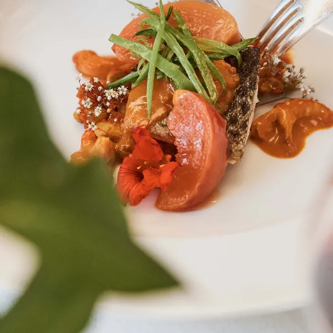 Gourmetgericht mit Fisch, Gemüse und essbaren Blüten in elegantem Restaurant