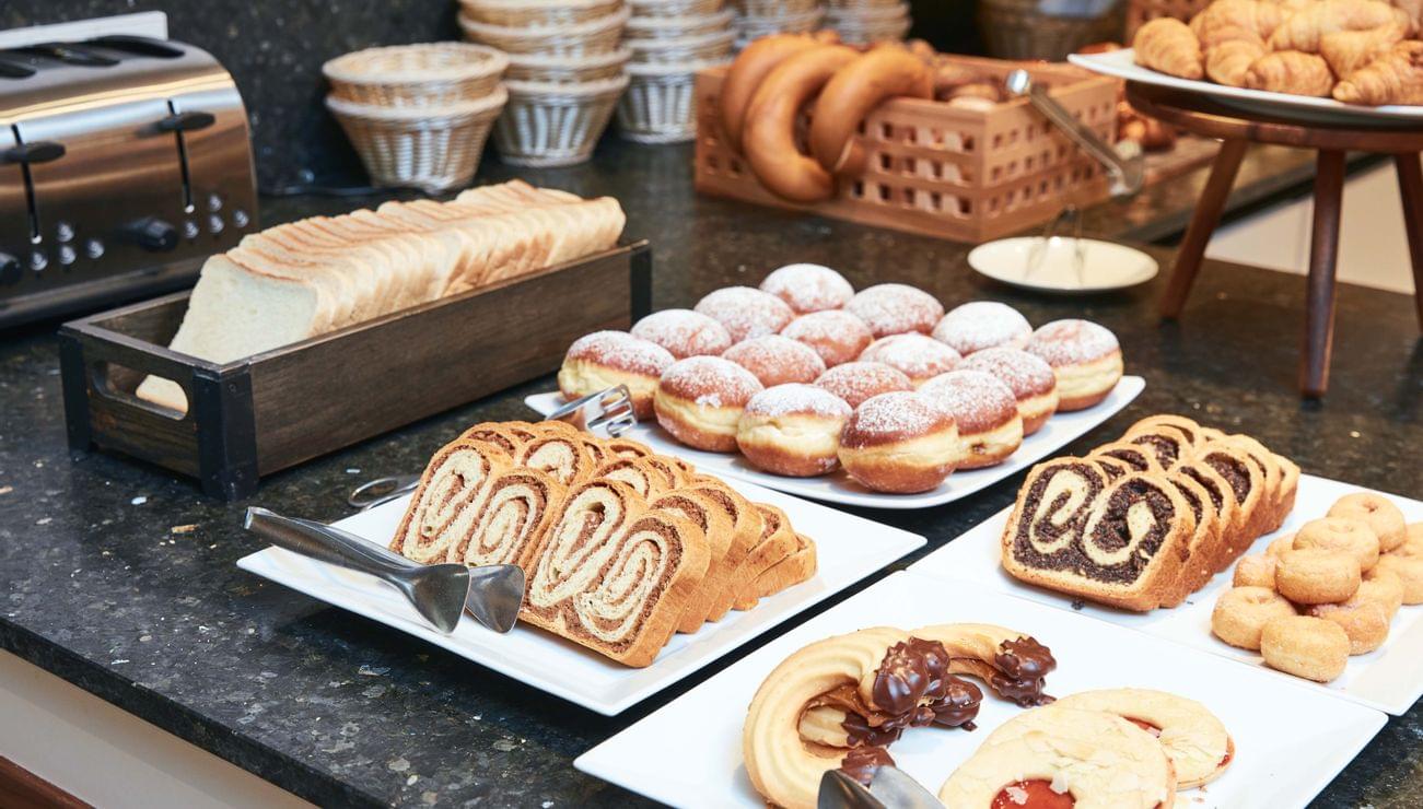 Breakfast buffet with sliced bread, jam cookies, donuts, and assorted pastries