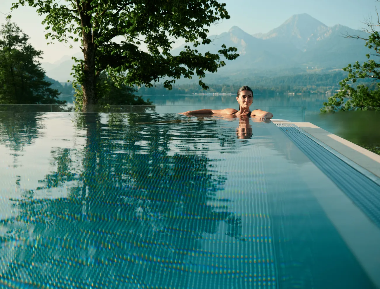 Frau entspannt in einem Infinity-Pool mit Blick auf eine Berg- und Seelandschaft