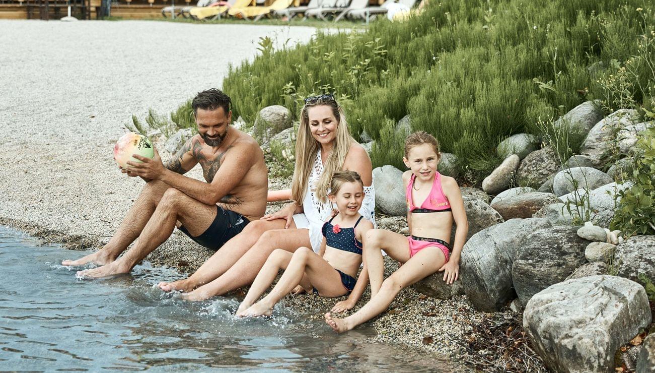 Glückliche Familie am Seeufer eines Strandresorts mit Sommerhütten im Hintergrund