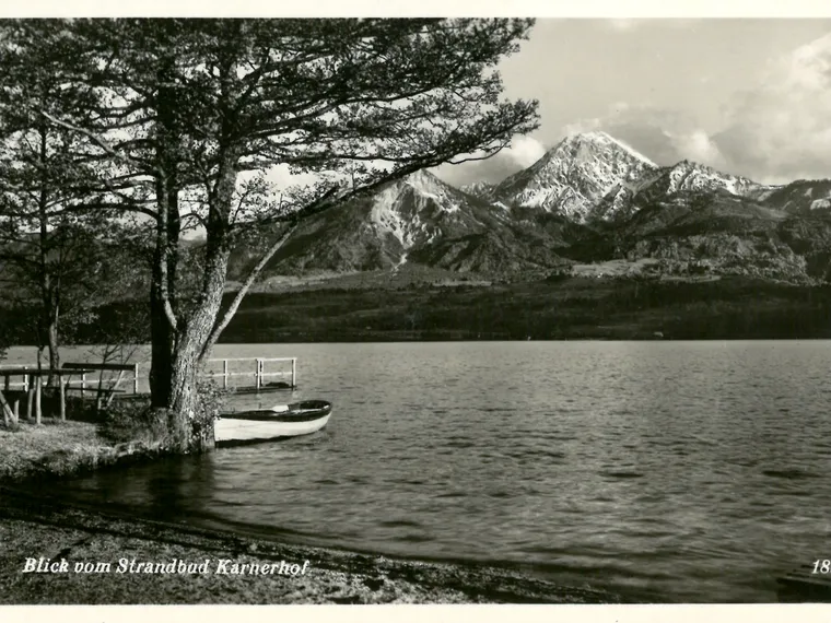 Lake view with dock, boat, trees and snow-capped mountains at Strandbad Karnerhof