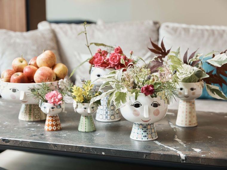 Decorative face-shaped ceramic vases with flowers and apples on a modern coffee table
