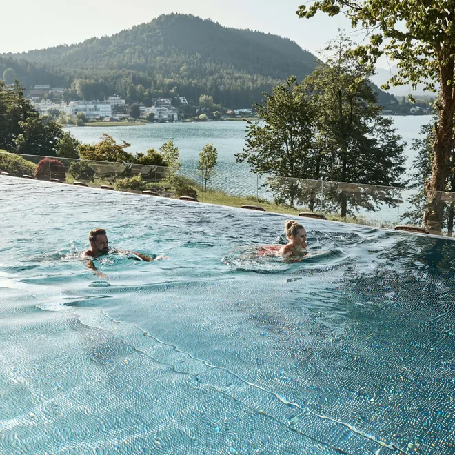 Coppia che nuota in piscina a sfioro con vista su lago e montagne boscose