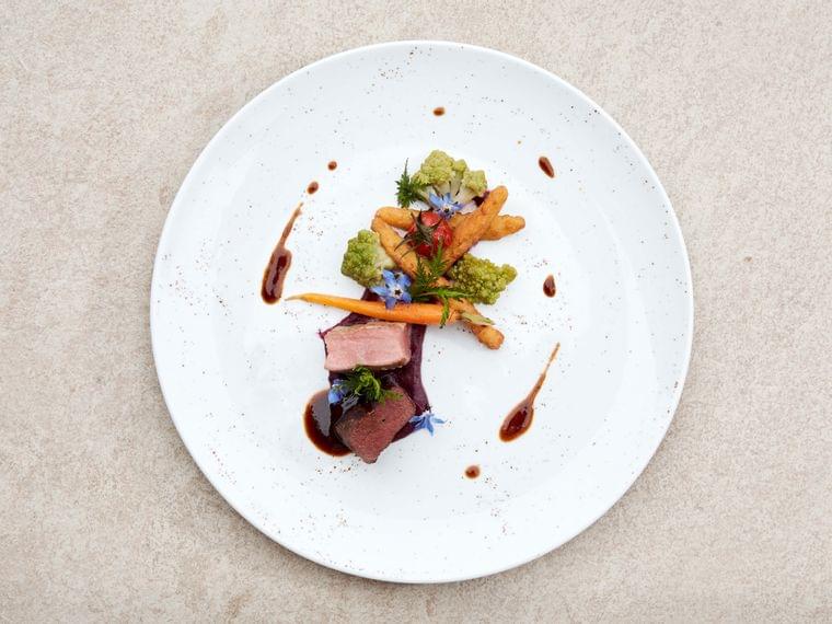 Gourmet plate with seared duck breast, Romanesco, baby carrot, sauce drizzle and edible flowers