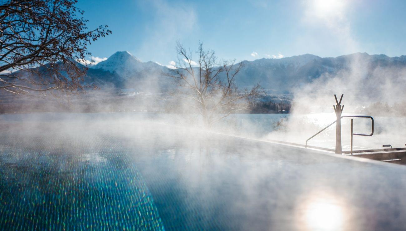 Vapore che sale da una piscina riscaldata all'aperto con vista sulle montagne innevate al sole