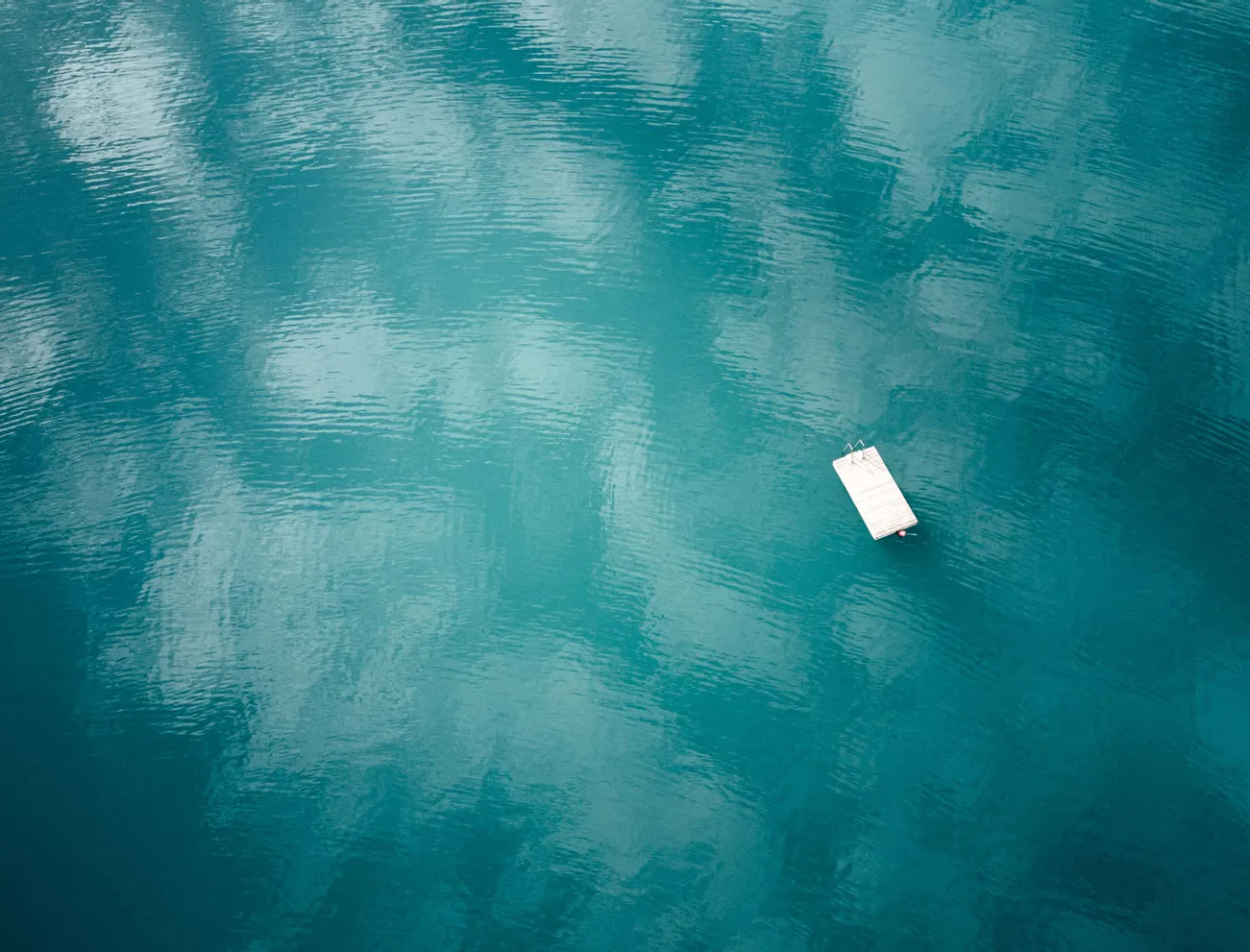 Floating wooden dock on calm turquoise lake with sky reflections