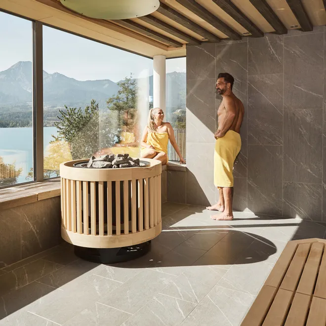 Coppia che si rilassa in una sauna moderna con vista panoramica su lago e montagne