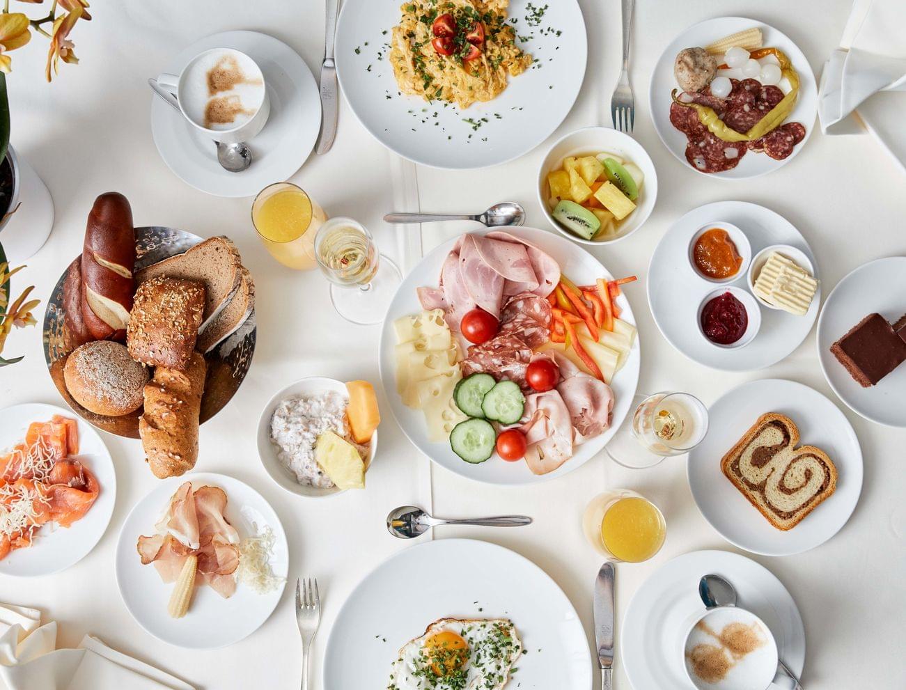 Kontinentales Frühstück mit Aufschnitt, Käse, Brot, Obst, Ei und Kaffee auf weißem Tisch
