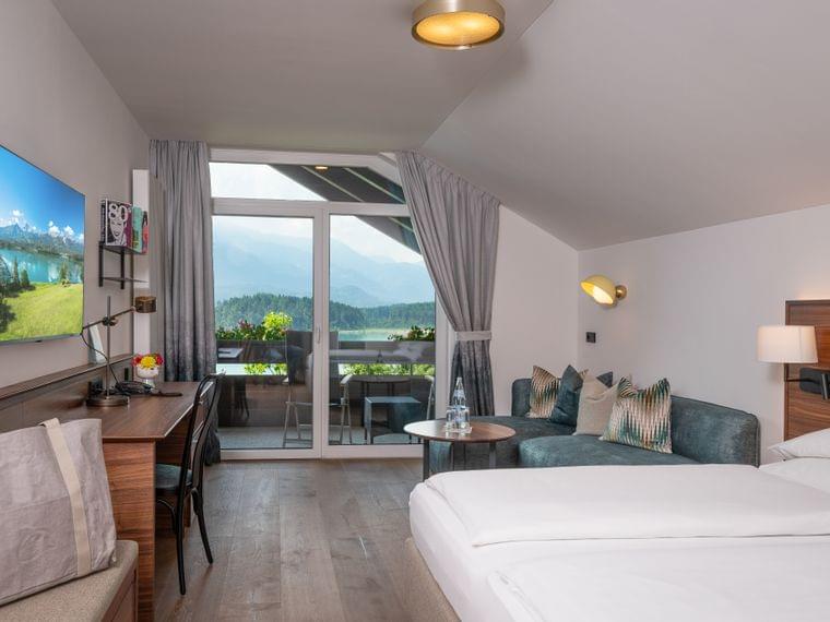 Modernes Hotelzimmer mit Balkon und Bergblick, Schreibtisch, Fernseher und gemütlicher Sitzecke